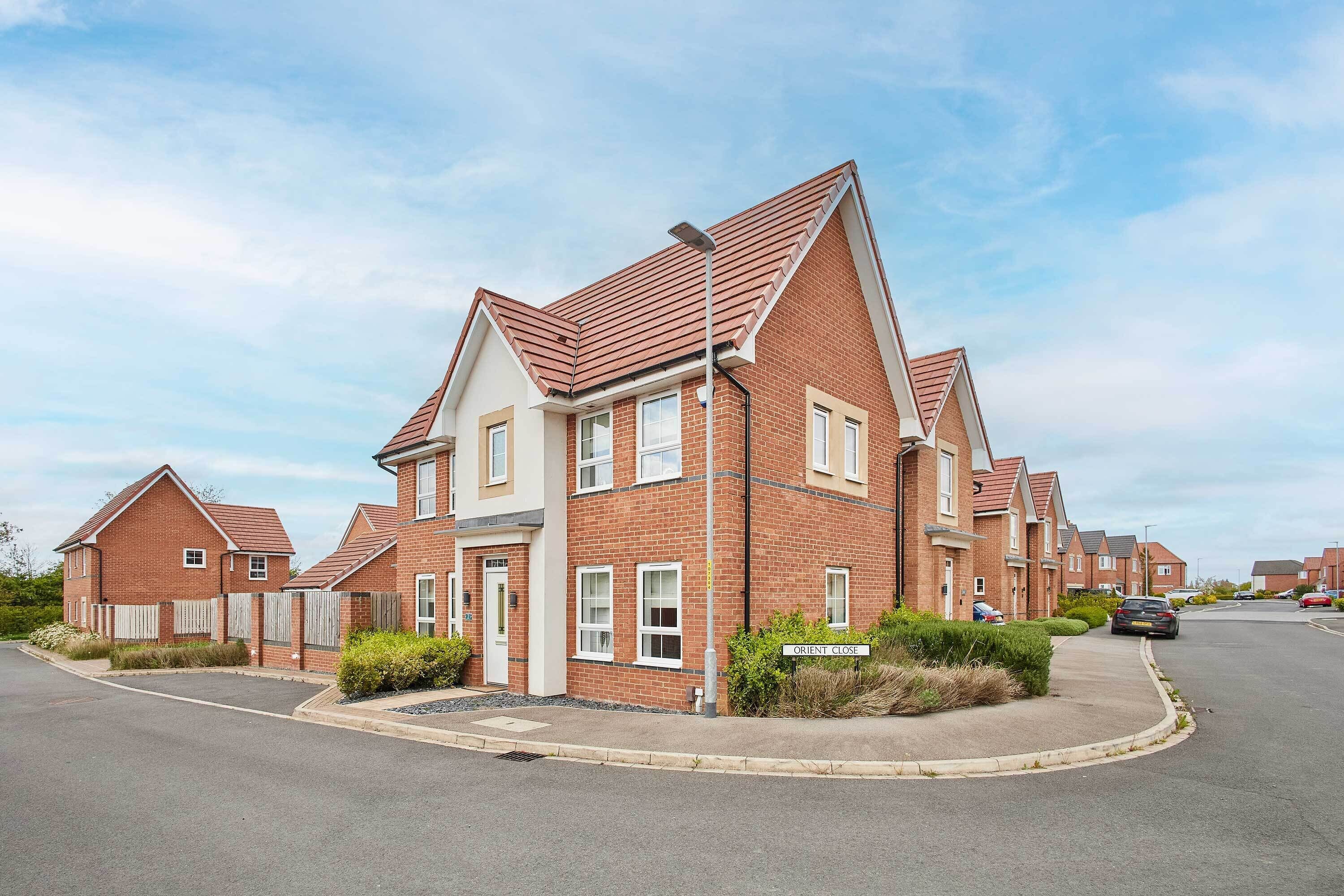 A row of modern brick houses with pitched roofs and a sign indicating 'ORIENT CLOSE'.