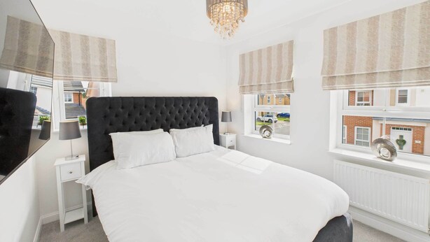 A bedroom with a large bed, a bedside table, a lamp, and a window with a view of buildings. - Host & Stay | Orient House (Yarm)