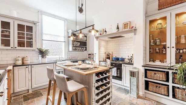 A modern kitchen with white cabinetry, a central island with bar stools, a wine rack, and a hanging light fixture. - Fabulous Solihull Luxury Designer Apartment 3BR (West Midlands)
