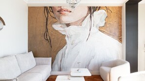 A modern living room with a large abstract painting, a white sofa, a small white table, and a wooden floor.