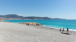 A pebble beach with a rocky outcrop and a clear blue sea.