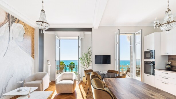 A modern living room with a wooden dining table, beige sofas, and a large painting.