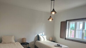 Ein Schlafzimmer mit zwei Betten, einem Fenster mit Vorhängen und einer Pendelleuchte.
