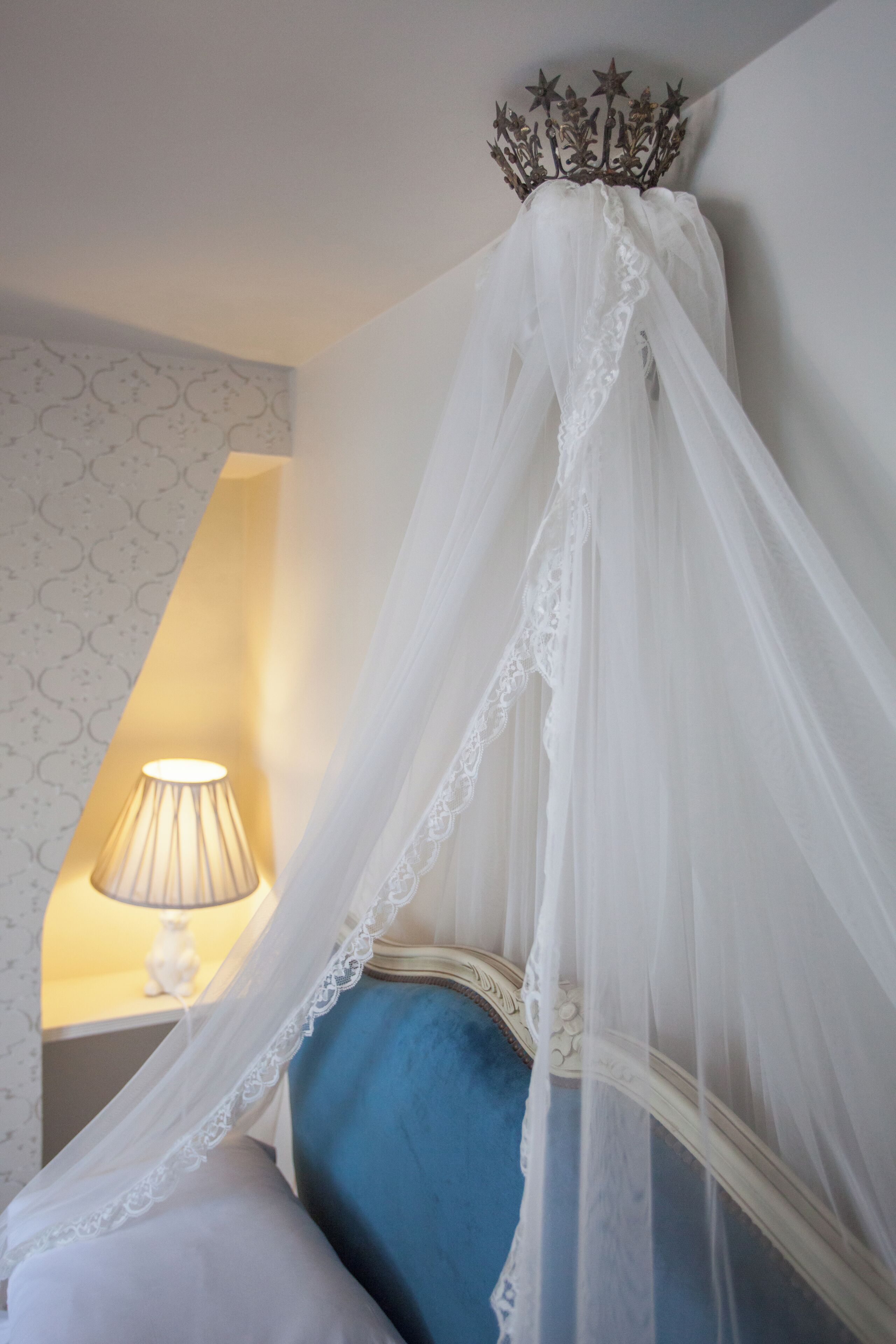 A bedroom with a canopy bed, a bedside lamp, and a patterned wallpaper.