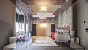 A modern hotel room with a bunk bed, a bedside table, a lamp, and a window with curtains. - Tide & Teacups (Brighton)