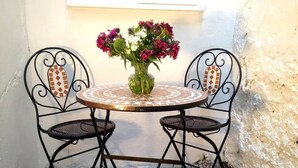 A small outdoor table with two chairs, a vase with flowers, and a white wall in the background. - Tide & Teacups (Brighton)