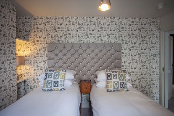 A double bed with a tufted headboard, two bedside tables, and patterned wallpaper.
