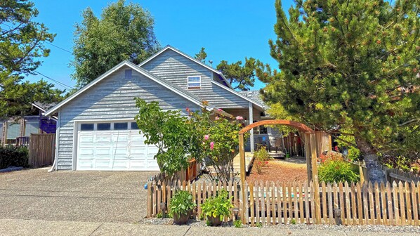 A two-story house with a garage, a wooden fence, and a garden with potted plants and a pergola.