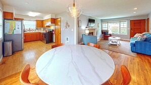 A modern kitchen with wooden cabinets, a stainless steel refrigerator, and a dining area with a marble table and wooden chairs.