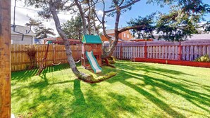 A backyard with a wooden playset, including a slide, and a fenced area.