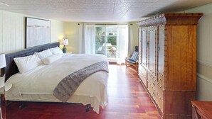 A bedroom with a large bed, a wooden wardrobe, and a view of the outdoors through a window. - Edgewood Escape at Seaside Beach (Seaside)
