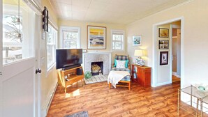 A living room with hardwood flooring, a fireplace, a television, and a sofa. - Sandpiper Cottage at Seaside Beach (Seaside)