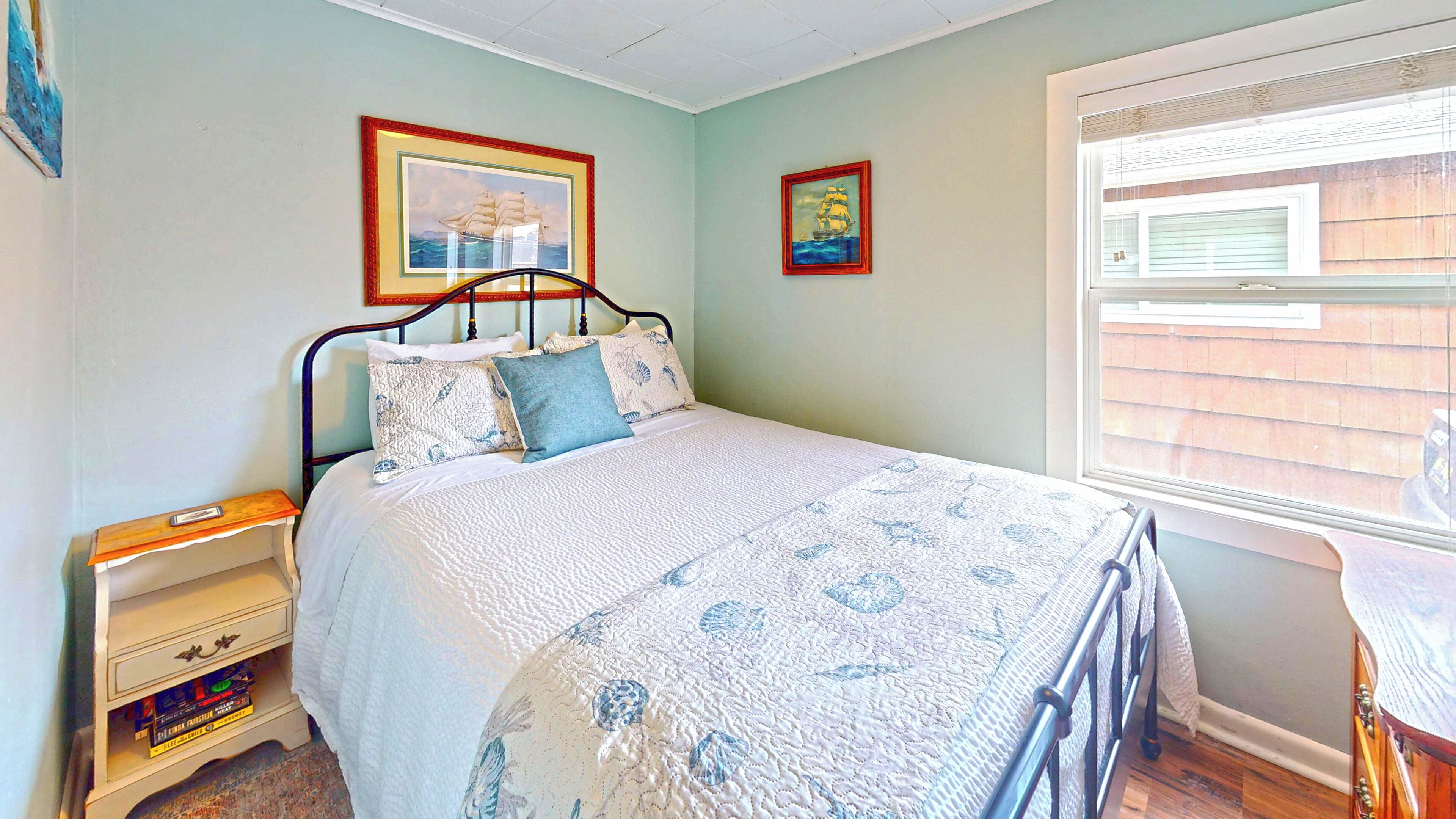 A neatly made bed with a patterned bedspread, a bedside table with a lamp, and two framed pictures on the wall.