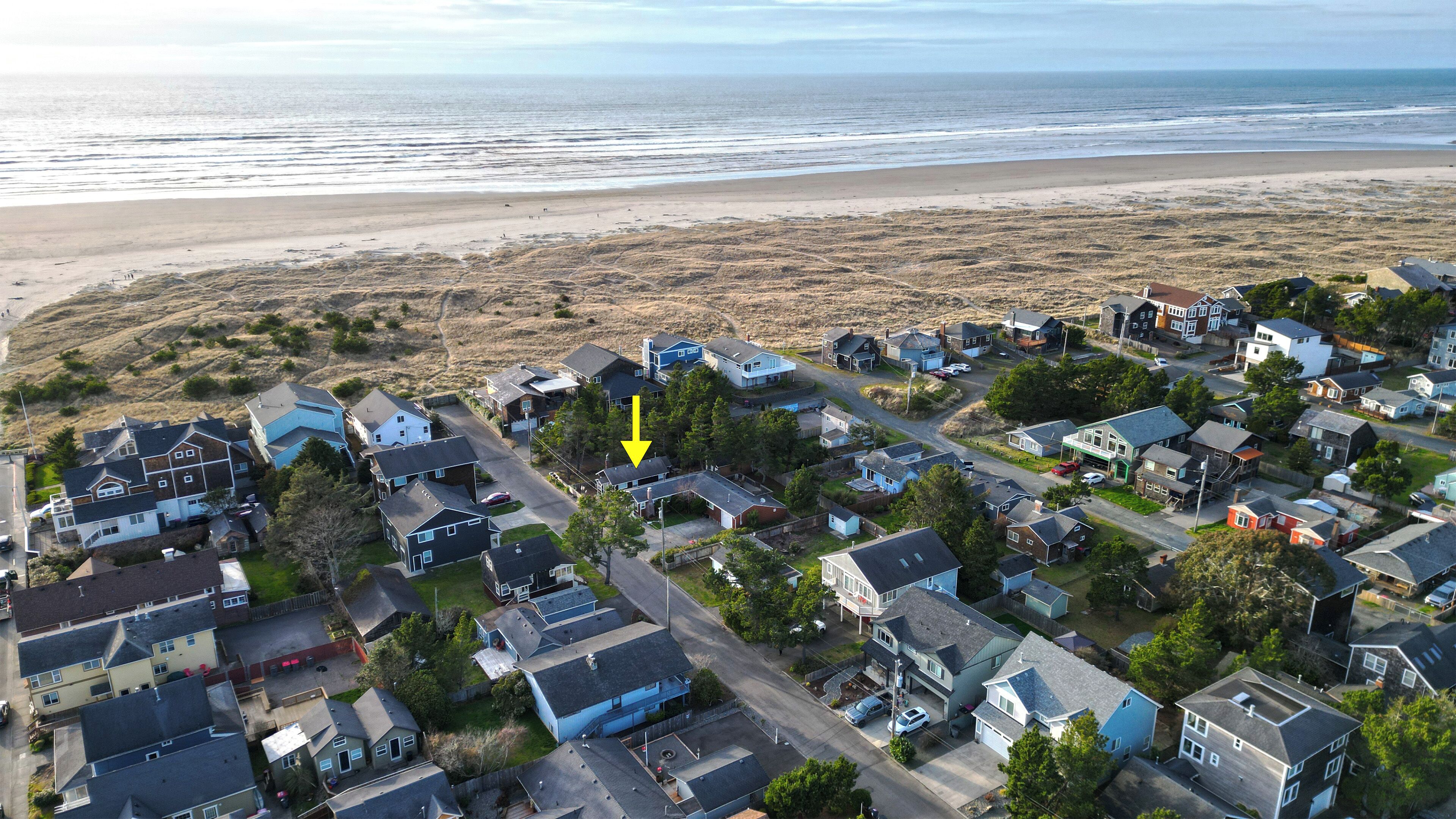 An aerial view of a coastal residential area with houses, a beach, and a road leading to the beach.