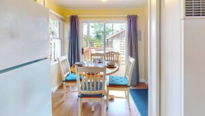 A dining area with a wooden table and chairs, a blue cushioned bench, and a view through a glass door to the outside. - Sandpiper Cottage at Seaside Beach (Seaside)