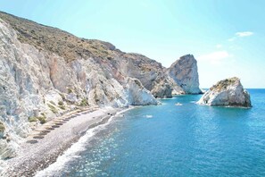 Un paisaje costero con acantilados rocosos, una playa de guijarros y aguas azul cristalino.