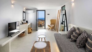 A modern living room with a sofa, a TV, a small table, and a view of the sea through an open door. - Amphora Thalassa Seaview Gem w/ Private Jacuzzi (Akrotiri)