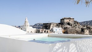 A white building with a pool, a bell tower, and a rocky hill with ruins. - Amphora Thalassa Seaview Gem w/ Private Jacuzzi (Akrotiri)
