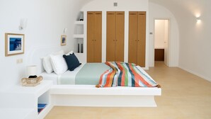 A bedroom with a bed, a bedside table, a lamp, a shelf with books, and a wardrobe. - Orasis House – Aegean Cave Retreat with Pool (Akrotiri)