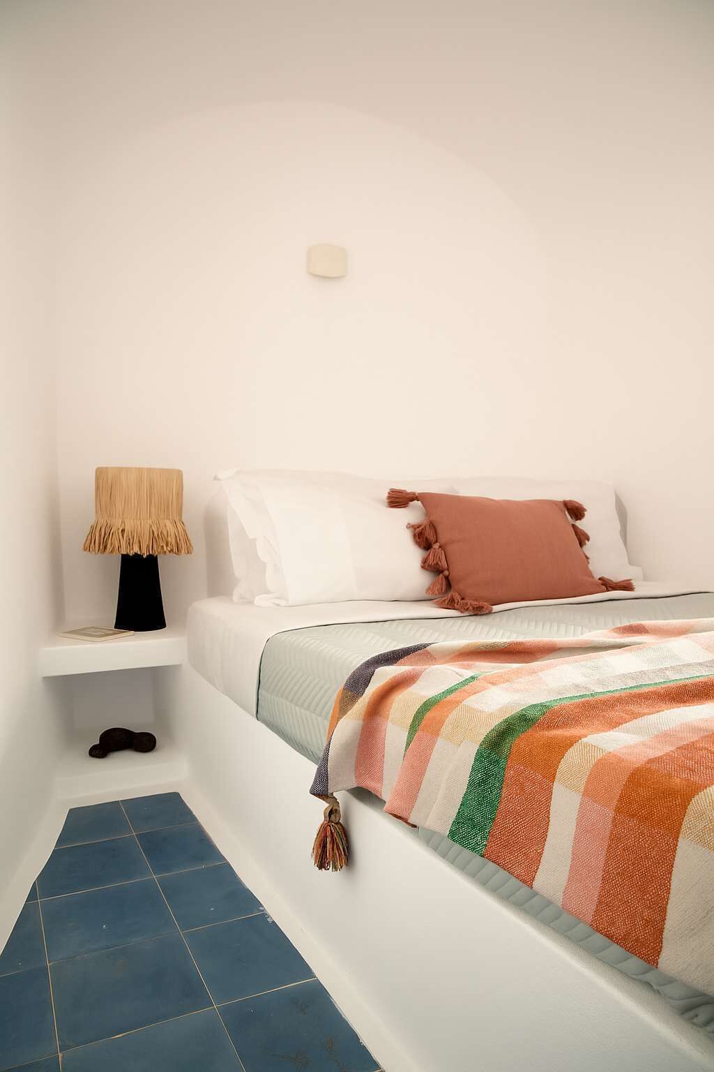 A bedroom with a bed, a nightstand, a lamp, and a blue tiled floor.