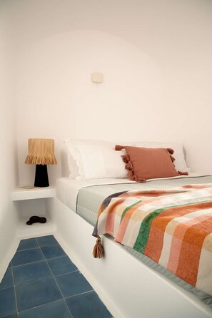 Quarto com cama, mesa de cabeceira, luminária e piso azul revestido com azulejos.