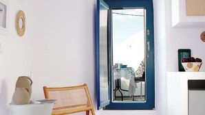 A room with a blue-framed window, a woven chair, a white table with a vase, and a colorful woven rug. - Orasis House – Santorini Retreat w/ Pool & Views (Akrotiri)