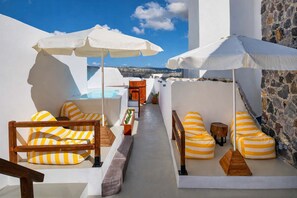 Une terrasse sur le toit avec des murs blancs, des éléments en pierre, des meubles en bois et des parasols blancs.