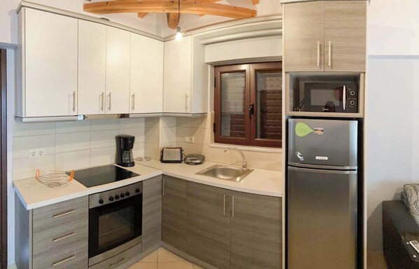 A compact kitchen with white cabinets, a built-in oven, a microwave, and a refrigerator.