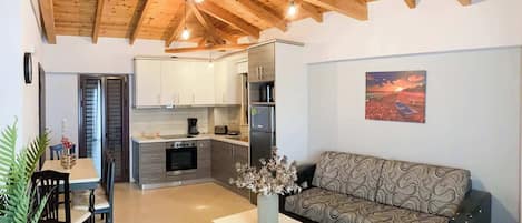 A modern living room with a sofa, a dining table with chairs, and a kitchen area with cabinets and appliances.