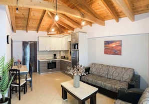 A modern kitchen with wooden beams, a dining area with a table and chairs, a sofa, and a painting on the wall.