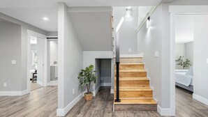 Un interior moderno con una escalera de madera, paredes de gris claro y una planta.
