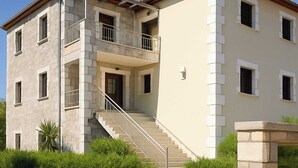 A two-story building with a balcony, a staircase, and a stone facade.