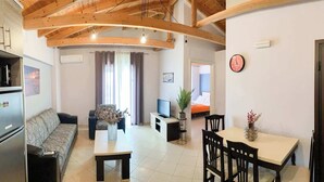 A modern living room with a sofa, a dining table with chairs, a TV, and a kitchen area with a refrigerator.