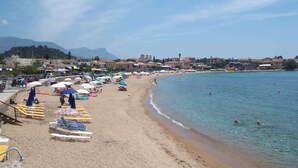 A beach with sun loungers and umbrellas, a clear sky, and buildings in the background.