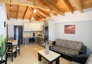 A modern kitchen with wooden beams, a dining area with a table and chairs, a sofa, and a painting on the wall.