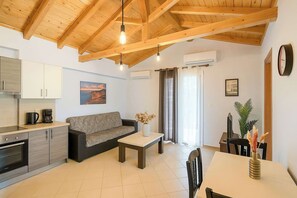 A modern kitchen with built-in appliances, a dining area with a table and chairs, a sofa, and a ceiling with exposed wooden beams. - Villa Orestis - Stoupa Seaview Getaway (Stoupa)