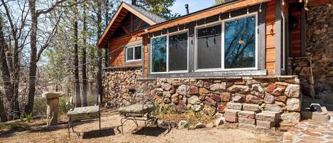Un chalet rustique aux murs de pierre, doté de grandes fenêtres et d’une terrasse en bois.