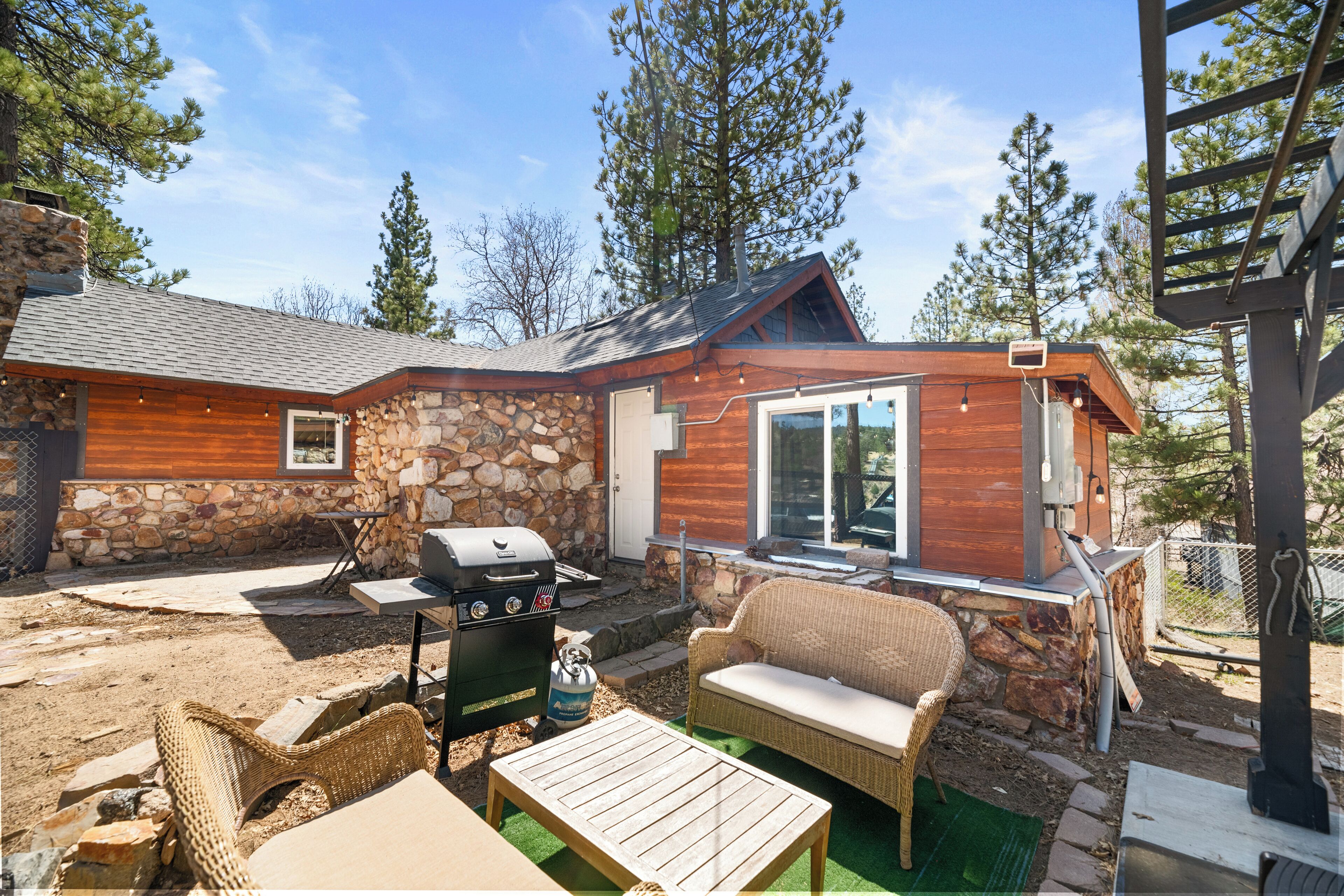 A stone and wood cabin with a patio area featuring a grill, wicker furniture, and a stone wall.