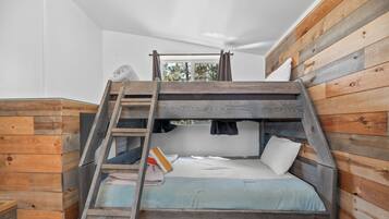 A bunk bed with a ladder, wooden walls, and a window with curtains.
