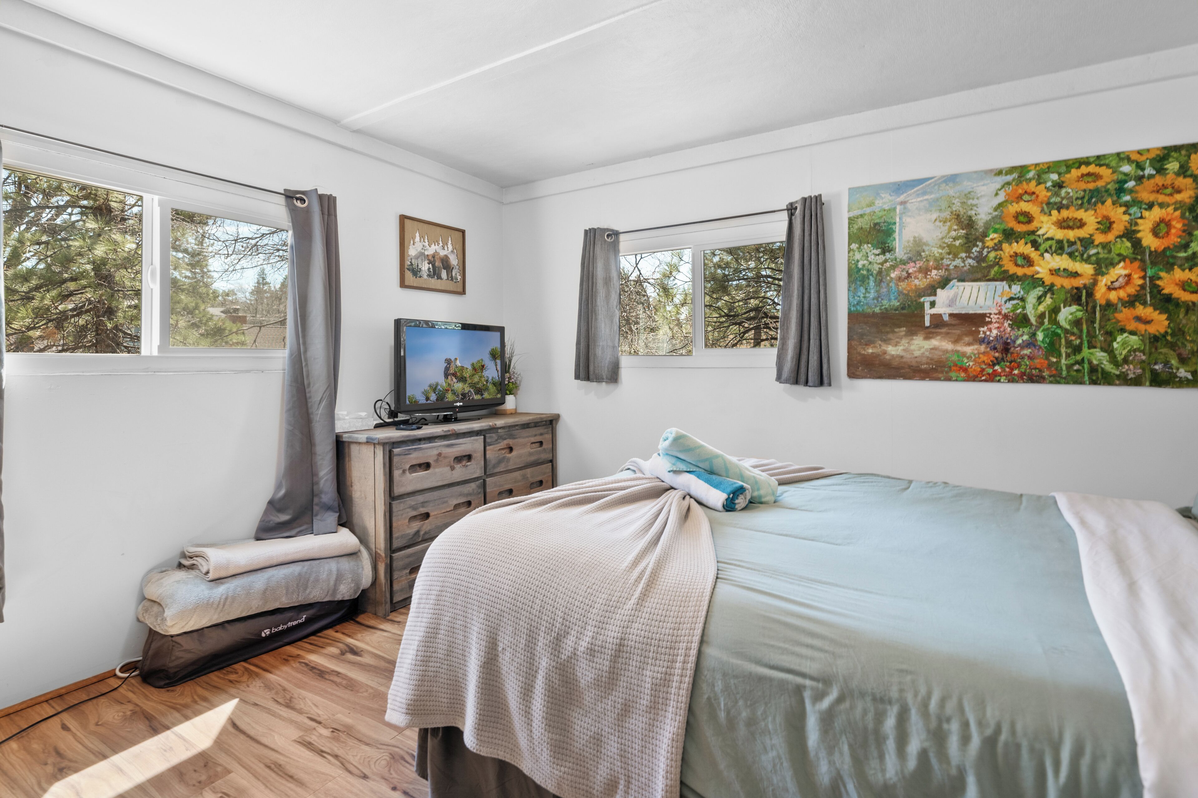 A bedroom with a bed, a TV, a dresser, and a painting of sunflowers.