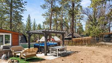 A covered outdoor seating area with a grill, chairs, and a table.