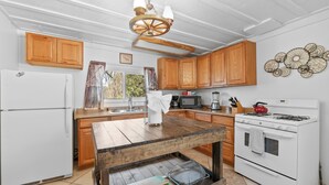 A kitchen with wooden cabinets, a white refrigerator, a stove, and a wooden table with a cutting board. - StoneHauz Cabin built in 1926 (Big Bear Lake)