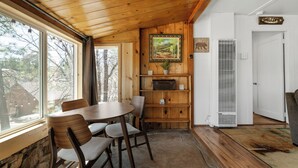 A wooden interior with a dining table and chairs, a fireplace, a welcome sign, and a view through a window. - StoneHauz Cabin built in 1926 (Big Bear Lake)
