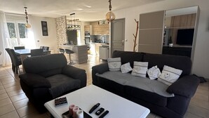 A modern living room with a sofa, a coffee table, and a dining area in the background.
