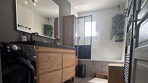 A compact laundry room with a washing machine, wooden cabinets, a mirror, and a ceiling light fixture.