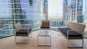 Ein moderner Balkon mit Glasgeländern, zwei Korbsufen mit Kissen und einem kleinen Tisch.