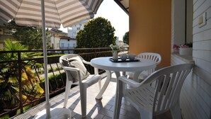 A balcony with white chairs, a striped umbrella, and a table with a pitcher, cup, and saucer. - Holiday stay in Bibione (Bibione)