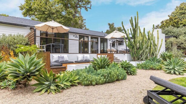 A modern house with a covered patio, outdoor seating, and a variety of plants.