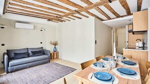 Una sala moderna con techo de madera, un sofá gris, una mesa de comedor para cuatro personas y una zona de cocina con microondas.