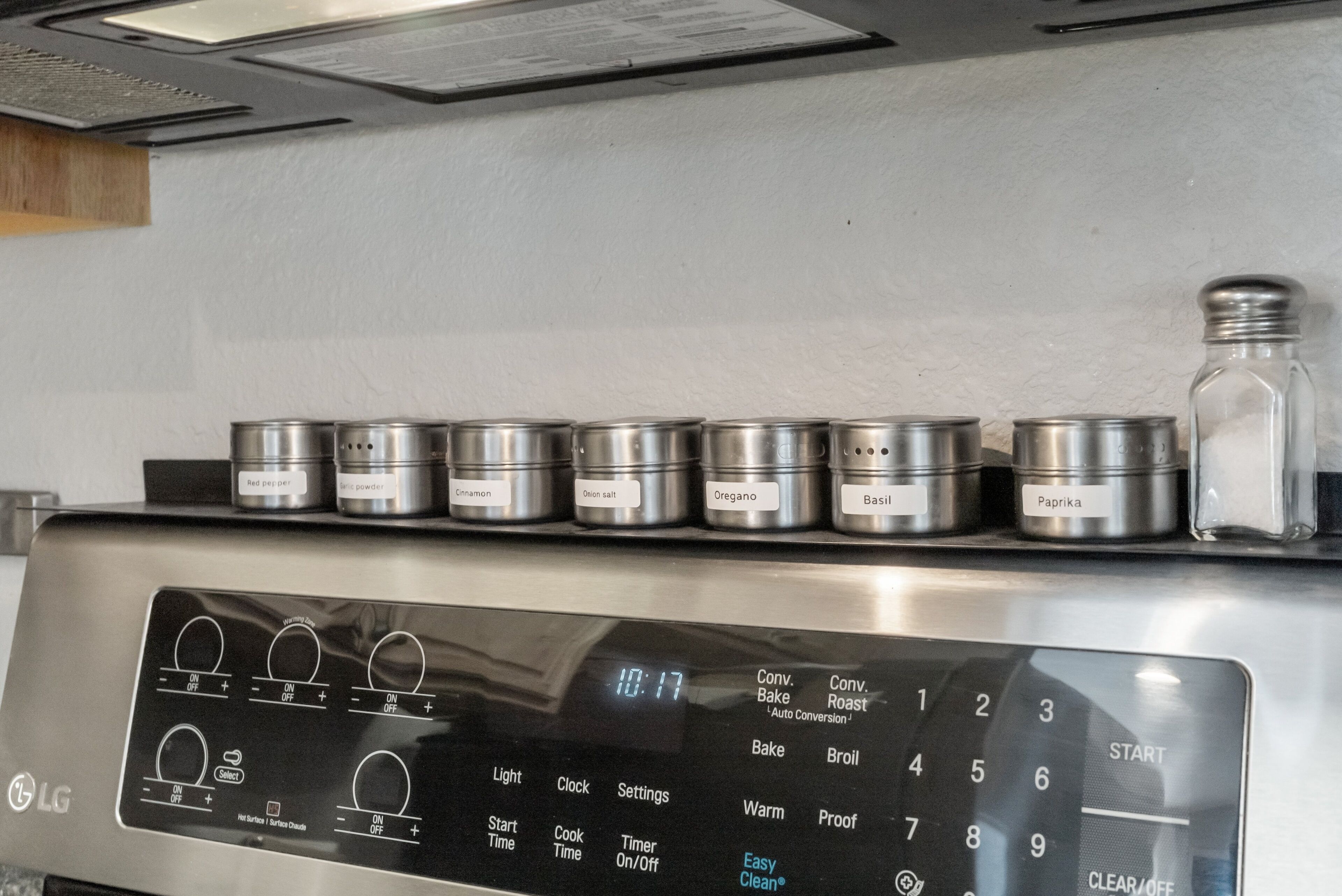 A kitchen with a digital clock displaying 10:17, various cooking settings, and spice containers labeled with different spices.